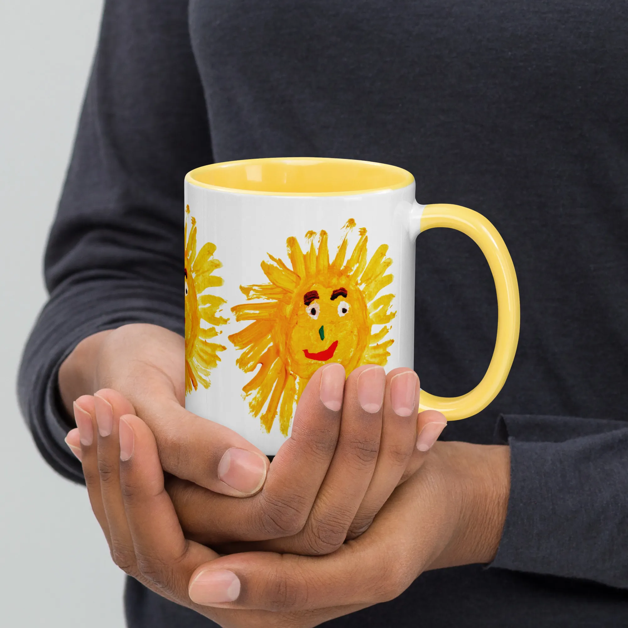 A hand holding the yellow painted sun mug by its comfortable rounded handle with a cozy winter sweater background